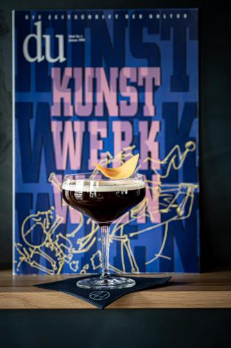 バーゼルにあるART HOUSE Basel - Member of Design Hotelsの本を片手にテーブルに座ったガラスのドリンク