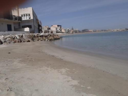 an empty beach with a building and the water at Suliccenti b&b Marzamemi in Marzamemi