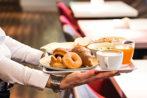 a person holding a tray of food with donuts and coffee at Hotel Ibis Milano Malpensa in Cardano al Campo