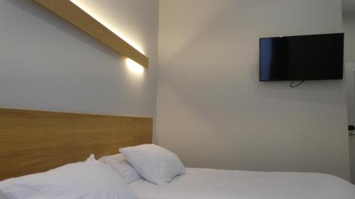 a bed with white sheets and a flat screen tv on a wall at Plaza Pombo B&B - Hostal in Santander