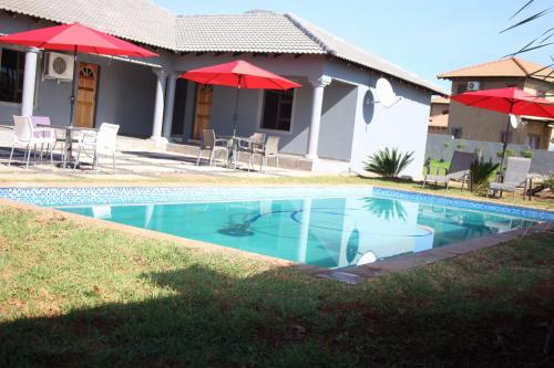 a swimming pool in front of a house with red umbrellas at Rufaro Hotel, Conference & Spa in Burgersfort