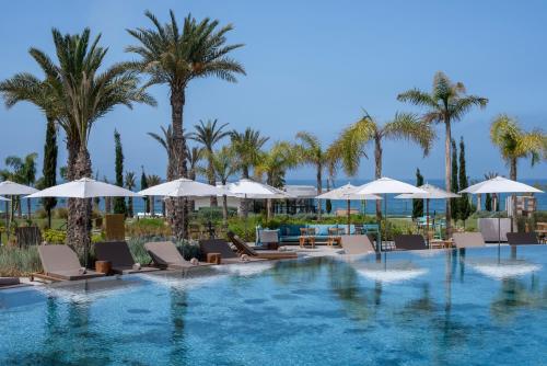 a pool with chairs and umbrellas and palm trees at Hyatt Regency Taghazout in Taghazout
