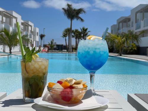 zwei Cocktails und eine Schale Obst auf einem Tisch neben dem Pool in der Unterkunft Island Home Fuerteventura in Corralejo