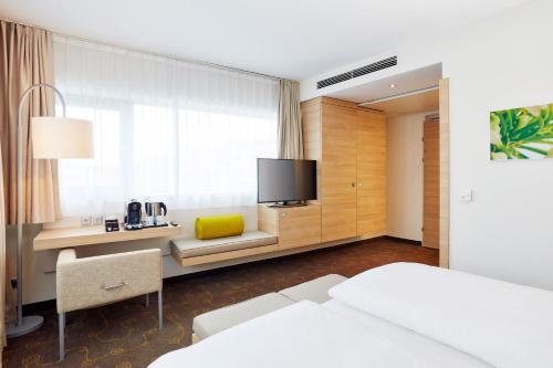 ザルツブルクにあるH+ ホテル ザルツブルクのベッド、デスク、テレビが備わるホテルルームです。