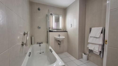 Baño blanco con bañera y lavamanos en Reigate Manor Hotel, en Reigate