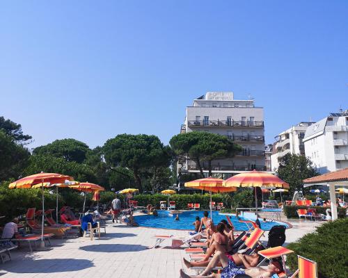 um grupo de pessoas sentadas ao redor de uma piscina com guarda-sóis em Hotel Ausonia em Milano Marittima