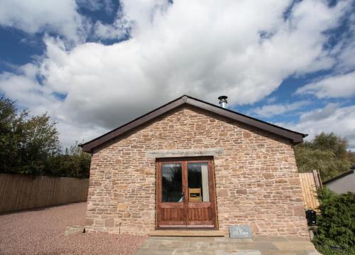 un pequeño edificio de ladrillo con puerta de madera en The Old Dairy - Boutique Countryside Cottage at Harrys Cottages en Pen y Clawdd