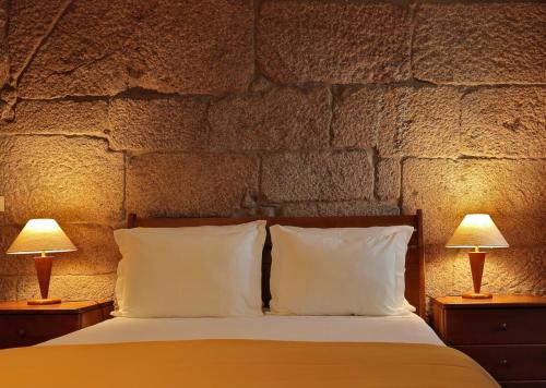 a bedroom with a stone wall with a bed and two lamps at Casa da Aldeia in Sever do Vouga