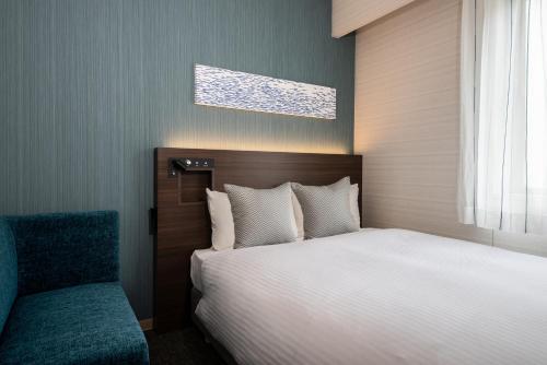 a bedroom with a bed and a blue chair at Hotel Vista Matsuyama in Matsuyama