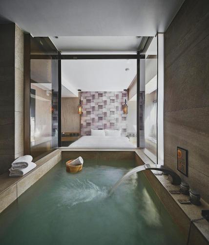 a bathroom with a bath tub with a bed in the background at JBG Hotspring Resort Hotel in Taipei