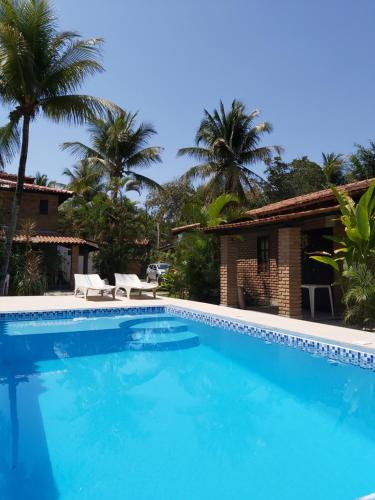 - une piscine en face d'une maison avec des palmiers dans l'établissement Golfinho Condomínio, à Arraial d'Ajuda