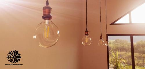 drie glazen lampen hangen aan de muur naast een raam bij Cabana Chalet Transylvania in Orlat