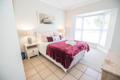 a bedroom with a bed with a red blanket and a window at Thirty River Club Villas managed by The Paper Fig House in Plettenberg Bay