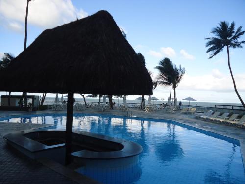 レシフェにあるGolden Beach Flat Recifeの藁の傘とビーチ付きのスイミングプール