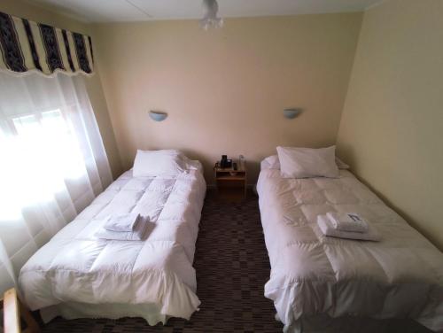 two beds in a room with white sheets at HOTEL GLACIARES in Puerto Natales