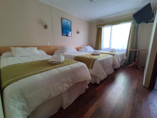 a hotel room with three beds and a window at HOTEL GLACIARES in Puerto Natales