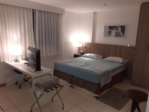 a bedroom with a bed and a desk and a television at Acomodação Tranquila (Centro de Campos) in Campos dos Goytacazes