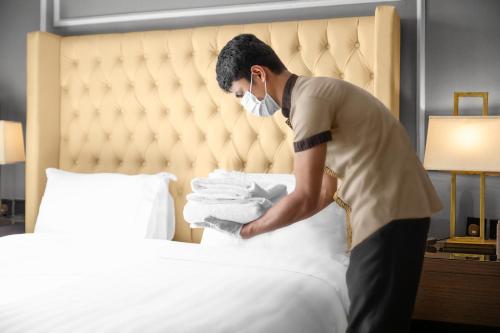 a man in a mask putting towels into a bed at Suknai Royal Hotel in Hail