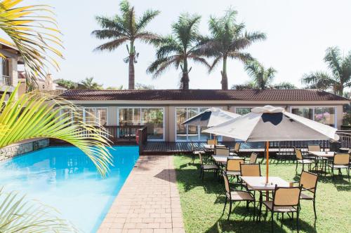 a pool with chairs and umbrellas next to a house at Umthunzi Hotel and Conference in Umtentweni