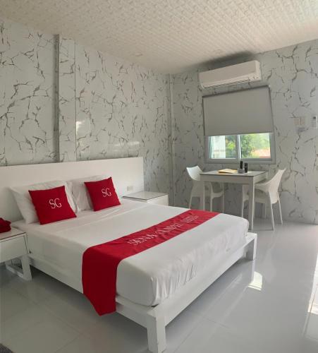 a white bedroom with a bed with red pillows and a desk at Sena Gladyz Suites in Panabo