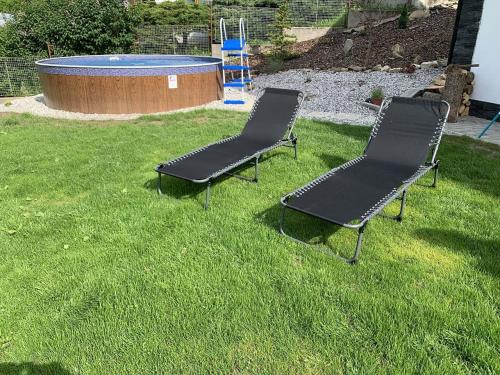 two chairs sitting in the grass next to a pool at Chata Nechata in Velhartice