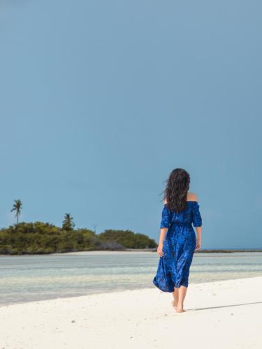 a woman in a blue dress walking on the beach at Shallow Lagoon Rasdhoo in Rasdu