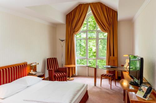 Cette chambre comprend un lit, un bureau et une fenêtre. dans l'établissement Dorint Herrenkrug Parkhotel Magdeburg, à Magdebourg