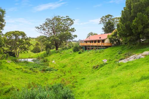 a house on a grassy hill with a river in front at Picturesque Pet-Friendly Farm Stay, Central Tilba , Near Mystery Bay! in Central Tilba