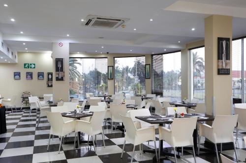 um restaurante com cadeiras brancas, mesas e janelas em Pavilion Hotel Durban em Durban