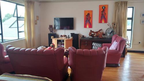 a living room with red chairs and a television at Goggas Nest BNB & Restaurant in Matsapha