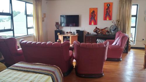 a living room with red chairs and a tv at Goggas Nest BNB & Restaurant in Matsapha