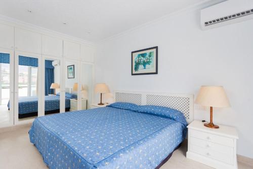een witte slaapkamer met een blauw bed en 2 lampen bij Penthouse 1801 mit fantastischem Blick im Precise Resort Tenerife in Puerto de la Cruz