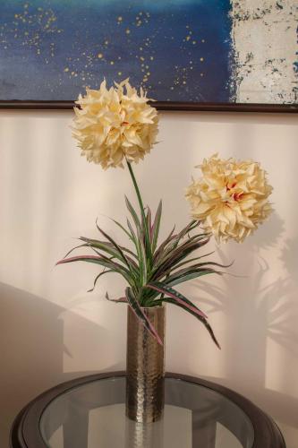 a vase with yellow flowers on a glass table at Hotel Alaya in Dehradun