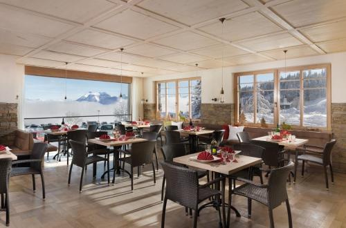 uma sala de jantar com mesas, cadeiras e janelas em Alpenhotel Bödele - Luxus Suite 23 em Schwarzenberg im Bregenzerwald