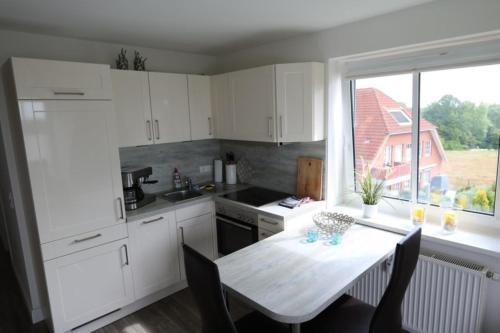 ティメンドルファー・シュトラントにあるFewo Sonnendeckの白いキャビネットとテーブル、窓付きのキッチン