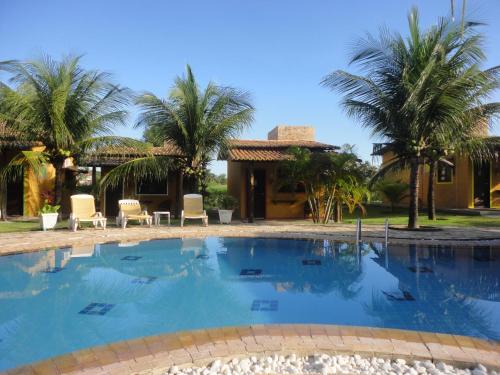 a swimming pool in front of a house with palm trees at Hotel Enseada Maracajaú in Maracajaú