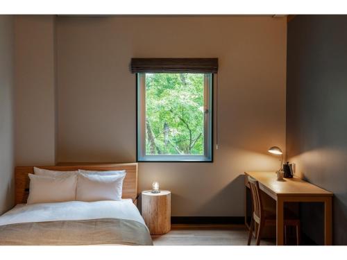 a bedroom with a bed and a desk and a window at HOTEL KARUIZAWA CROSS - Vacation STAY 56455v in Karuizawa