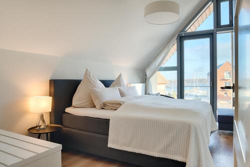 a bedroom with a white bed with a large window at Ostsee - Reetdachhaus Nr 32 "Sonnendeck" im Strand Resort in Heiligenhafen