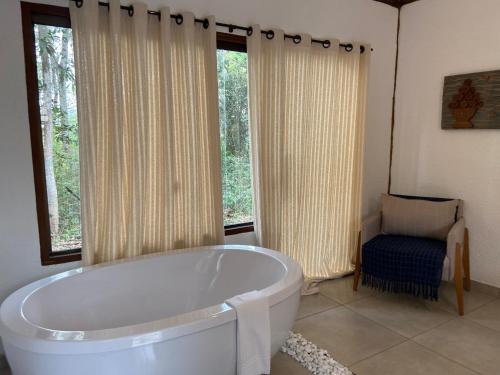 ein Badezimmer mit einer Badewanne, einem Stuhl und Fenstern in der Unterkunft A Mi Manera Pousada , cerveja própria e Bistrô ! in Brumadinho