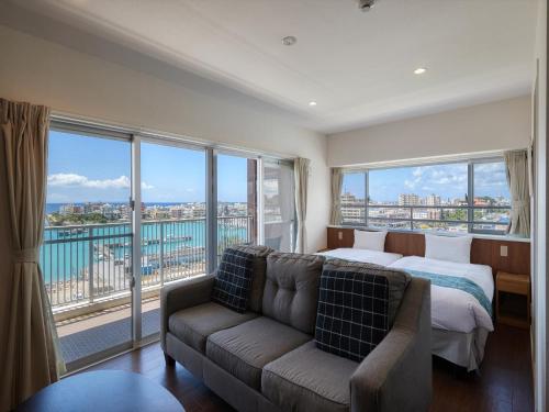a bedroom with a bed and a couch and windows at Seaside Condominium Rana Chatan in Chatan