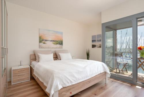 ein weißes Schlafzimmer mit einem Bett und einem Balkon in der Unterkunft Ostsee - Maisonette - Appartement Nr 48 "Hafenblick" im Strand Resort in Heiligenhafen