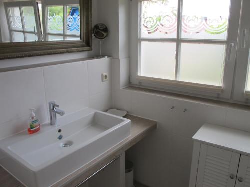 a white bathroom with a sink and two windows at DHH Wiesenstraße 55 - Dünensand in Zingst