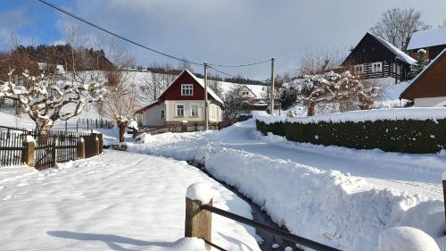 a yard covered in snow with a house in the background at Chata u potoka in Lázně Bělohrad