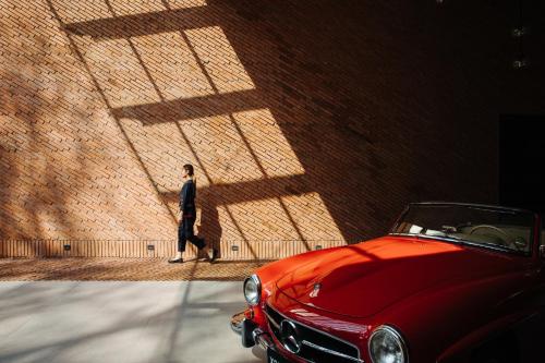 a man standing next to a brick wall with a red car at Cross Chiang Mai Riverside in Chiang Mai