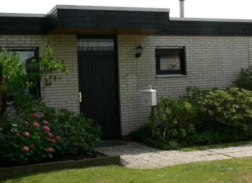 uma casa com uma porta preta e algumas flores em Bungalow 451 in Tossens em Tossens