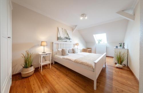 a white bedroom with a bed and two potted plants at Sturmmöwe in Westermarkelsdorf