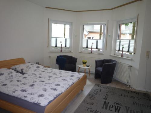 a bedroom with a bed and two chairs and windows at Ferienzimmer Alte Kämpe in Heede