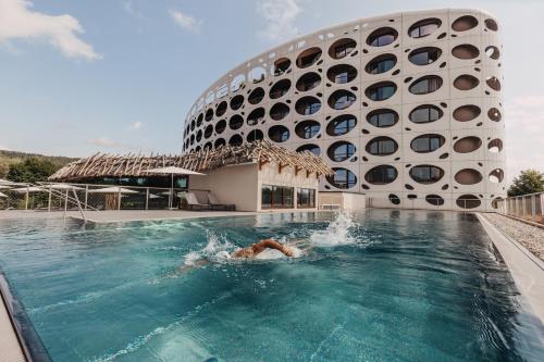 una persona che nuota in una piscina di fronte a un edificio di Seepark Wörthersee Resort a Klagenfurt