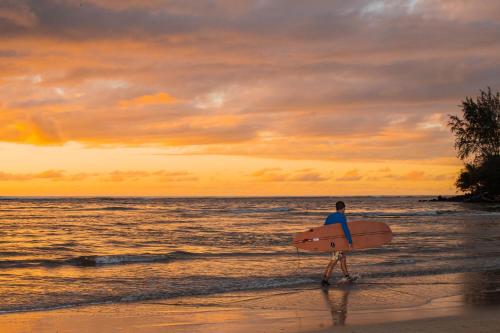 a man walking on the beach with a surfboard at Hanalei Beach House Estate home in Hanalei