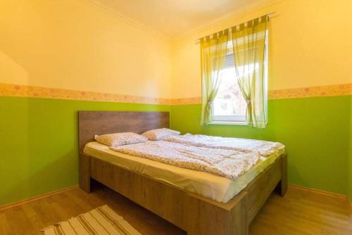 een slaapkamer met een bed met groene muren en een raam bij Zalán apartmann in Balatonkeresztúr